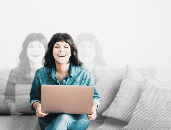 Young woman sits on couch at her laptop laughing at the camera.