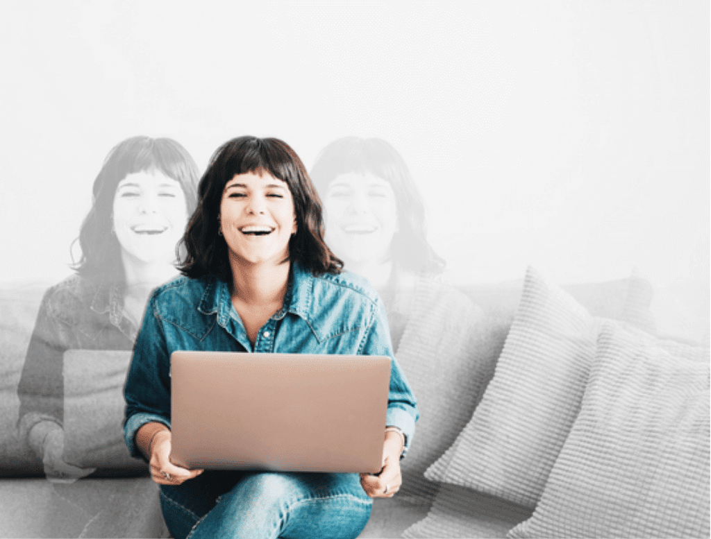 Young woman sits on couch at her laptop laughing at the camera.